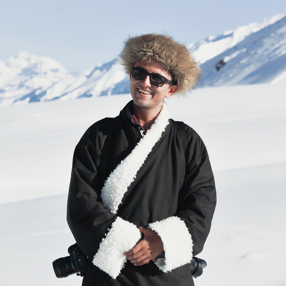 Himanshu Khagta in a traditional robe and fur hat, standing in the snow with his camera
